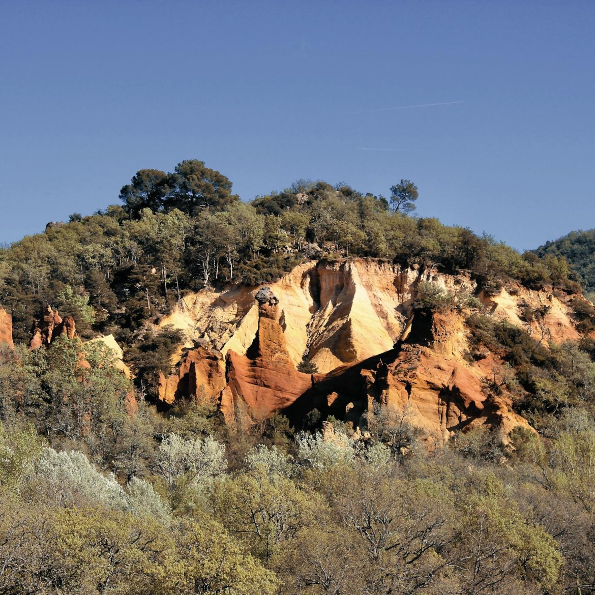 Stunning ochre cliffs surrounded by lush greenery in Rustrel, Provence, France.